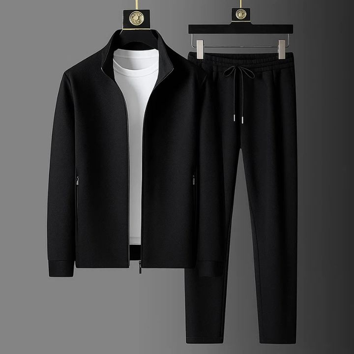 Schwarzer Herren-Zweiteiler mit Stehkragen, Reißverschlussjacke und Hose mit Kordelzug in strukturierter Optik.