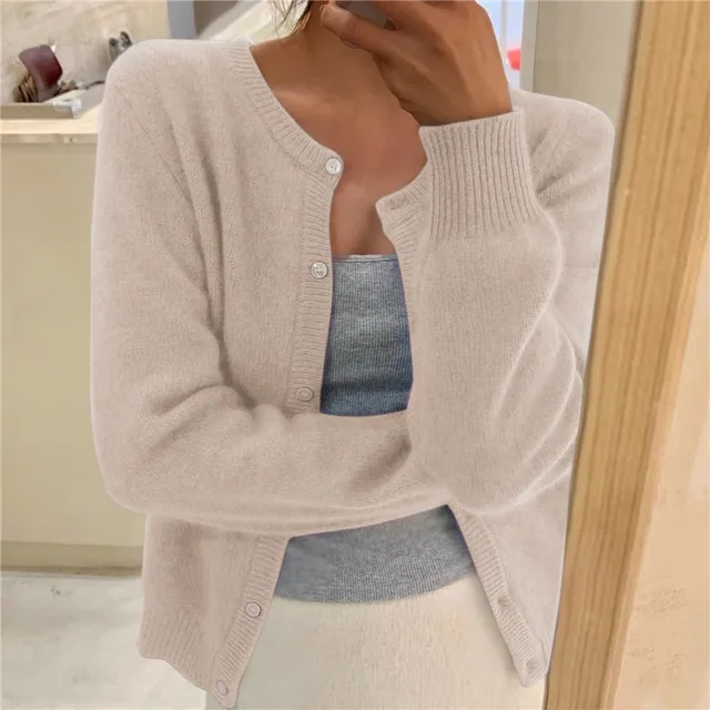 Beigefarbene Damen-Strickjacke mit Rundhalsausschnitt, Knopfleiste und gerippten Bündchen vor einem Spiegel.