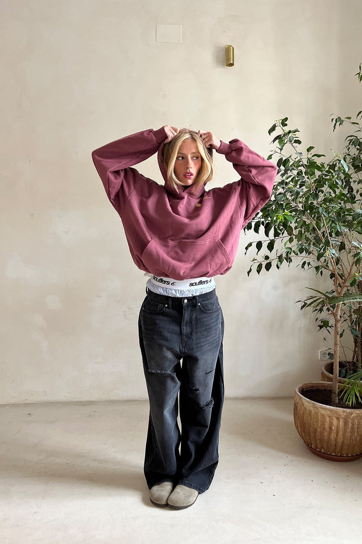 Frau trägt einen weinroten Oversized-Hoodie mit Kapuze und Kängurutasche zu einer schwarzen, weit geschnittenen Jeans.