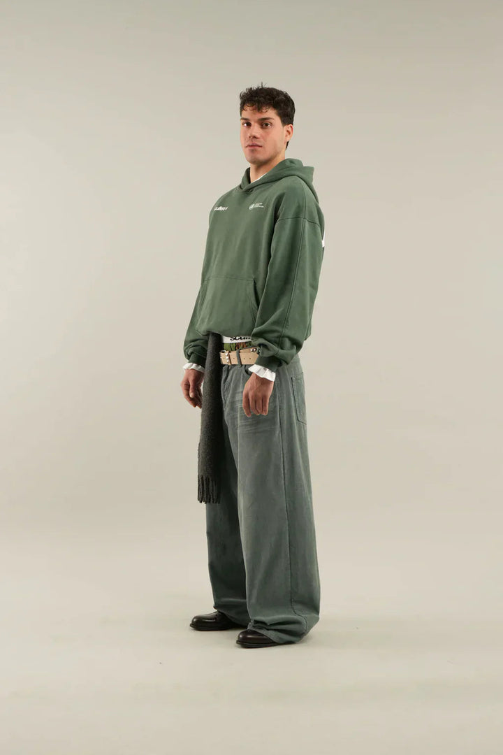 Dunkelgrüner Oversized-Hoodie mit Kapuze, Kängurutasche und weißem Logo-Print, kombiniert mit weiter Hose.