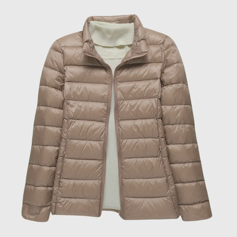 Beigefarbene, leicht gesteppte Damenjacke mit Reißverschluss und hohem Kragen über einem hellen Rollkragenpullover.