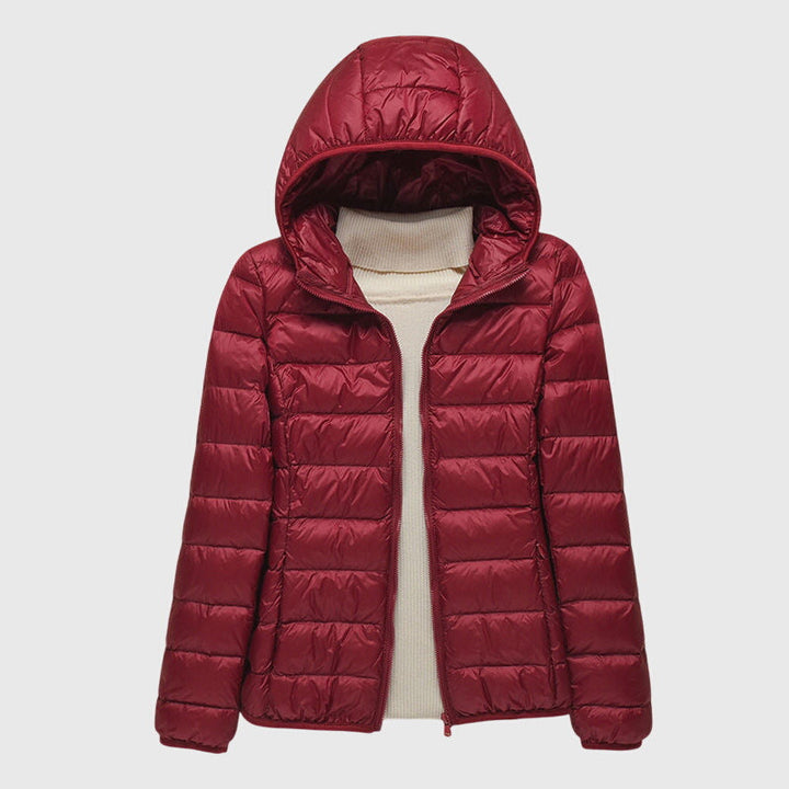Dunkelrote, leicht gesteppte Damenjacke mit Kapuze und durchgehendem Reißverschluss über einem beigen Rollkragenpullover.