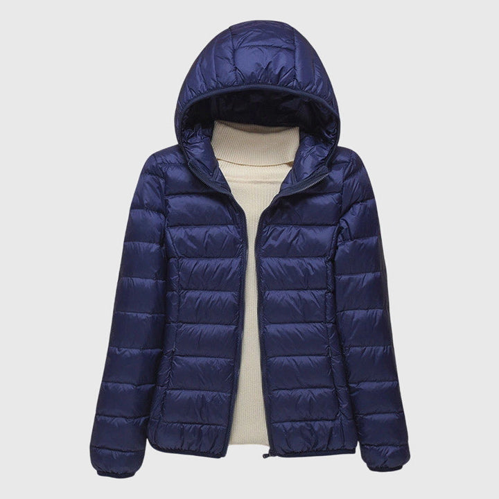 Dunkelblaue, leicht gesteppte Damenjacke mit Kapuze und Reißverschluss über einem beigen Rollkragenpullover.