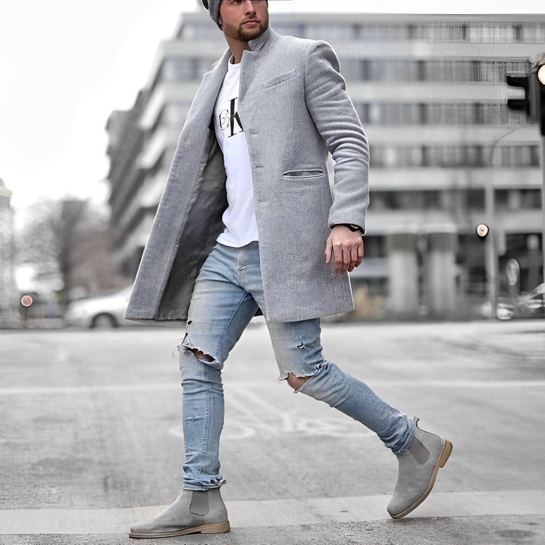 Grauer Slim-Fit Herrenmantel mit Stehkragen, kombiniert mit weißem T-Shirt, zerrissenen Jeans und grauen Chelsea Boots.