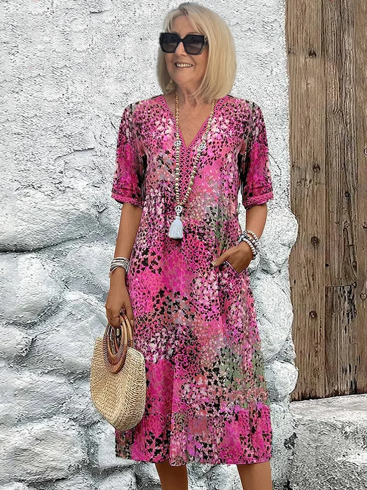 Rosa Midikleid mit V-Ausschnitt, kurzen Ärmeln, floralem Muster und Seitentaschen, getragen mit einer Strohtasche.