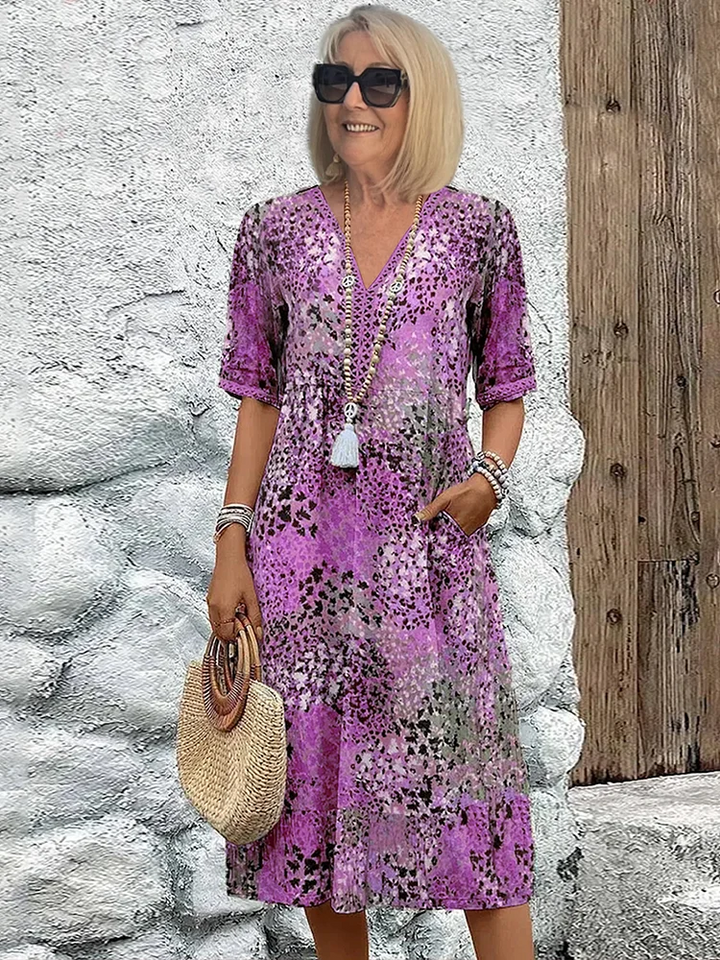 Lila Midikleid mit Blumenmuster, V-Ausschnitt, kurzen Ärmeln und praktischen Seitentaschen für einen sommerlichen Look.