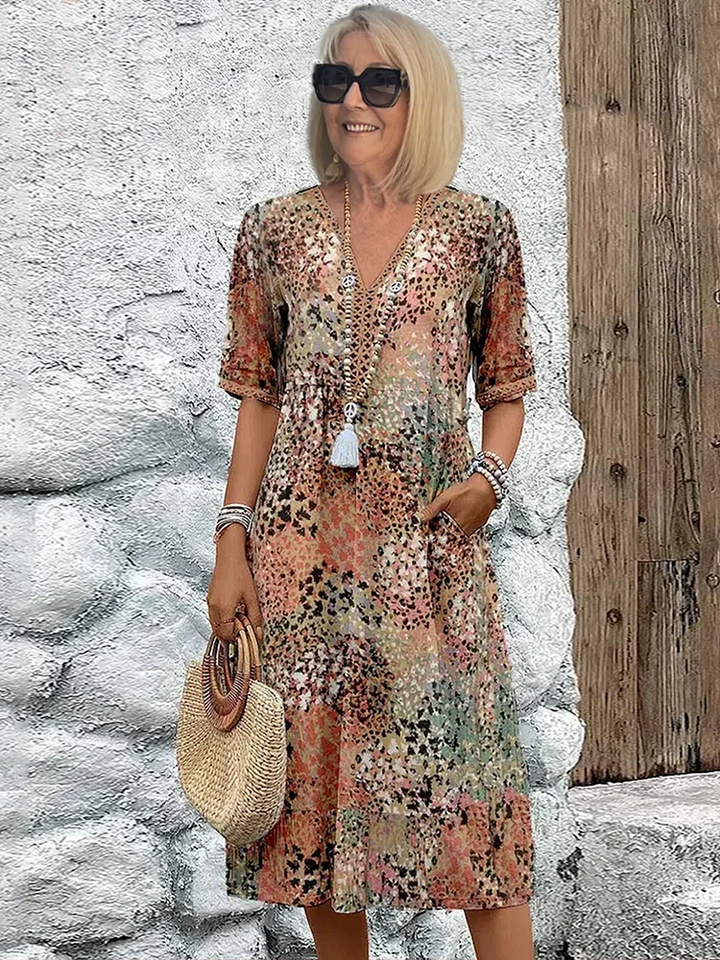 Frau trägt ein buntes Midikleid mit V-Ausschnitt, Blumenmuster, kurzen Ärmeln und praktischen Seitentaschen.