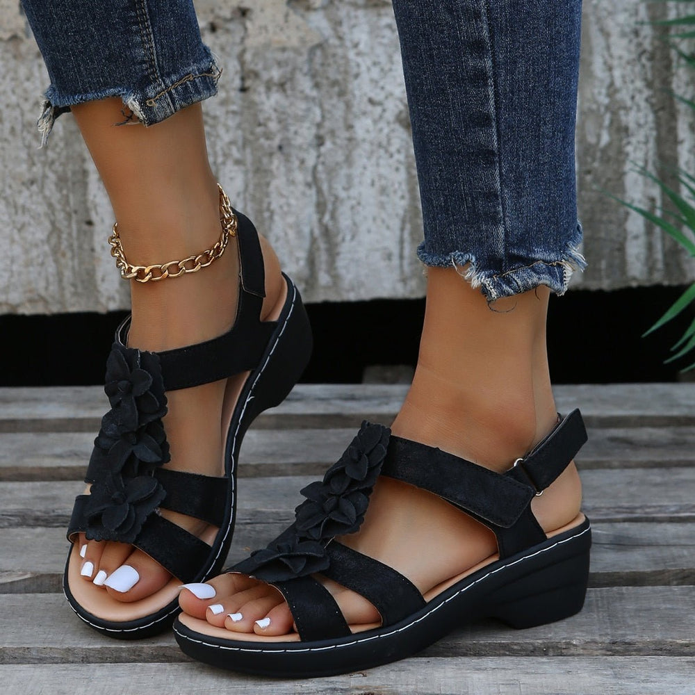Schwarze Clara Keilsandalen mit dekorativen Blüten und Riemen zu einer Jeans getragen.
