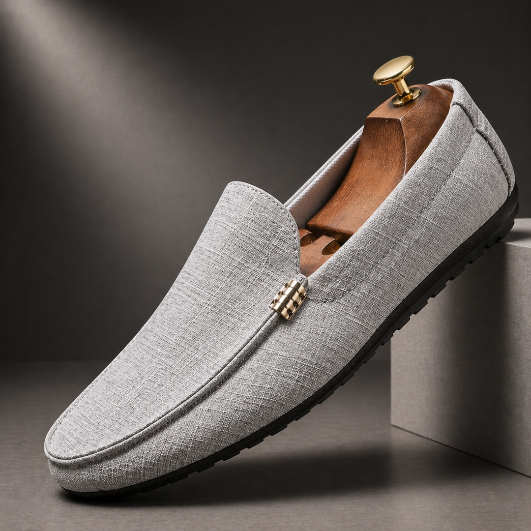 Grauer Herren-Slip-On-Loafer aus strukturiertem Canvas mit schwarzer Sohle und elegantem Metalldetail auf einem Schuhspanner.