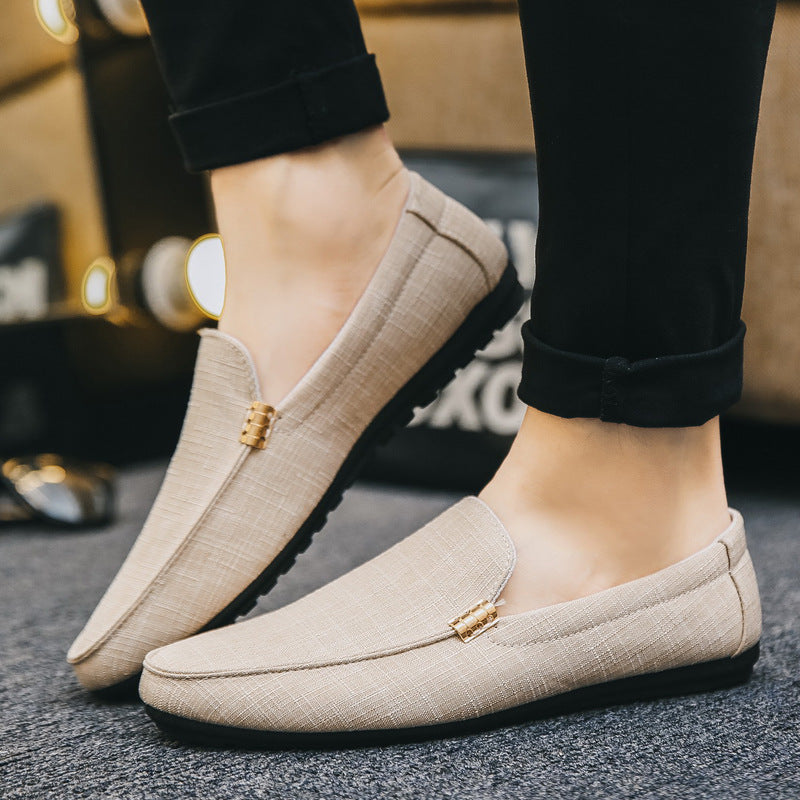 Beigefarbener Herren-Slip-On-Loafer aus strukturiertem Canvas mit flacher schwarzer Sohle und dezenten Metalldetails.