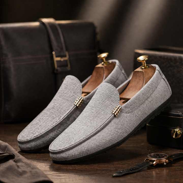 Graue Herren-Slip-On-Loafer aus strukturiertem Canvas mit flexibler Sohle und elegantem Design auf dunklem Holzhintergrund.