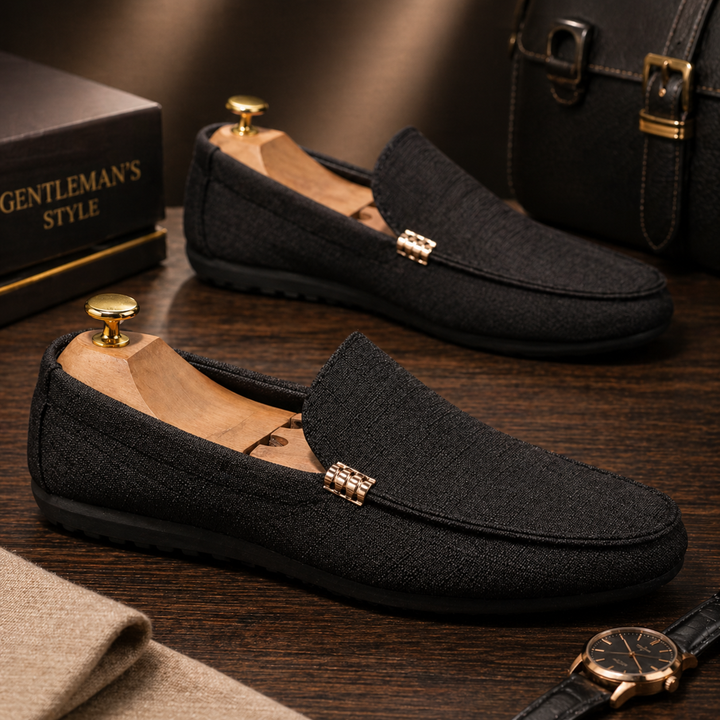 Schwarzer Herren-Loafer aus strukturiertem Canvas mit goldenem Zierelement in schlichter Slip-On-Optik.