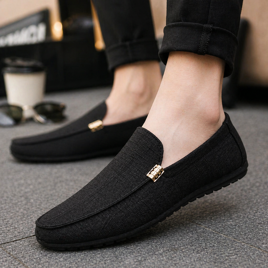 Schwarzer Herren-Loafer aus strukturiertem Canvas mit Slip-On-Design und dekorativem goldenem Metallelement.