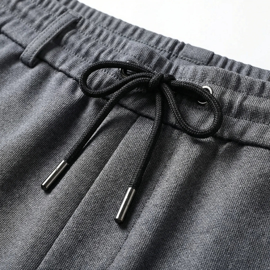 Dunkelgraue Herrenhose mit elastischem Komfortbund, schwarzem Kordelzug und hochwertigen Metallabschlüssen.