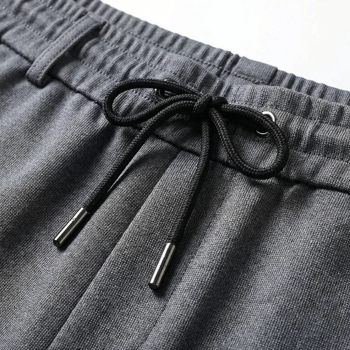 Dunkelgraue Herrenhose mit elastischem Komfortbund, schwarzem Kordelzug und hochwertigen Metallabschlüssen.