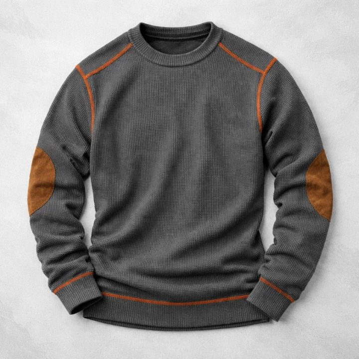 Dunkelgrauer Waffelstrick-Pullover mit Rundhals, braunen Ellbogen-Patches und kontrastierenden orangefarbenen Nähten.