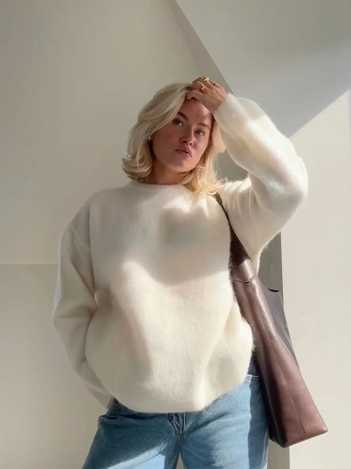 Flauschiger, cremeweißer Damenpullover mit Rundhals in lockerer Passform, kombiniert mit blauen Jeans und einer Tasche.