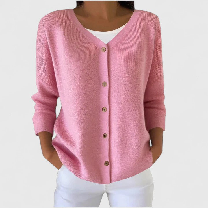 Rosa Strickjacke mit V-Ausschnitt, Knopfleiste und gerippten Details, getragen zu einer weißen Hose.