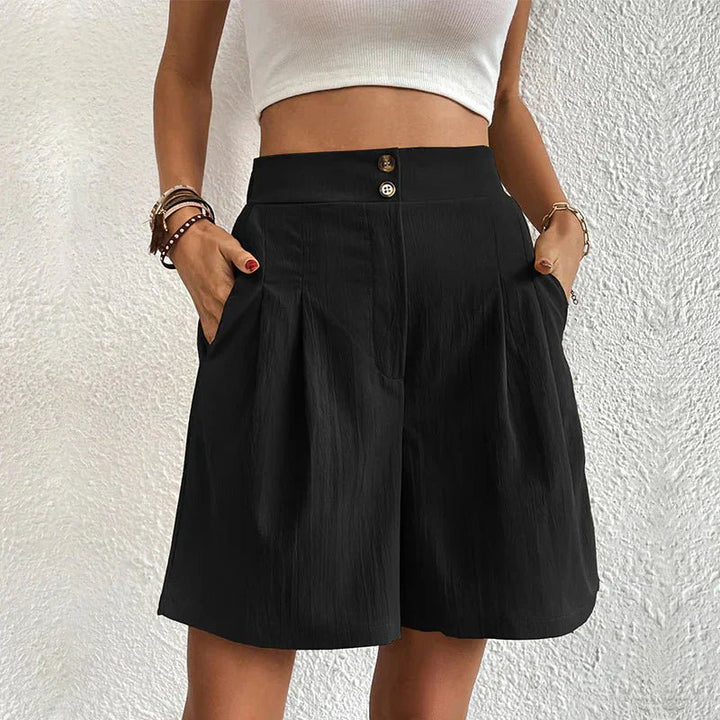 Schwarze High Waist Shorts mit Bundfalten, weitem Bein, Seitentaschen und doppelter Knopfleiste am hohen Bund.