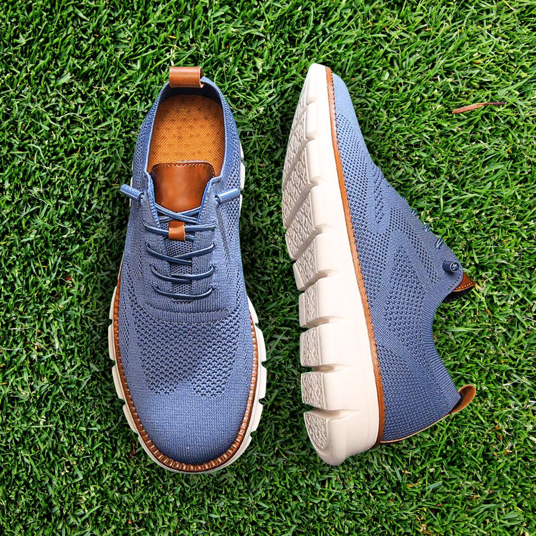 Blauer Fabian Herren-Mesh-Sneaker mit braunen Lederdetails und weißer, flexibler Laufsohle auf grünem Rasen.