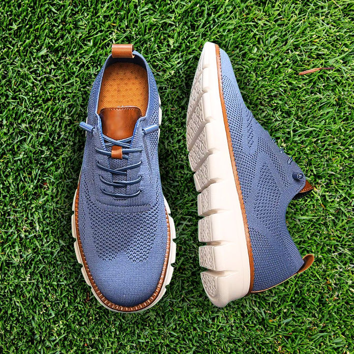 Blauer Fabian Herren-Mesh-Sneaker mit braunen Lederdetails und weißer, flexibler Laufsohle auf grünem Rasen.