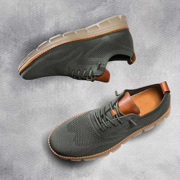 Olivgrüner Herren-Mesh-Sneaker mit braunen Lederoptik-Details und flexibler, heller Laufsohle auf grauem Hintergrund.