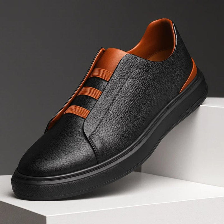 Schwarzer Herren-Sneaker aus genarbtem Leder mit orangefarbenen Elastikbändern und robuster schwarzer Laufsohle.