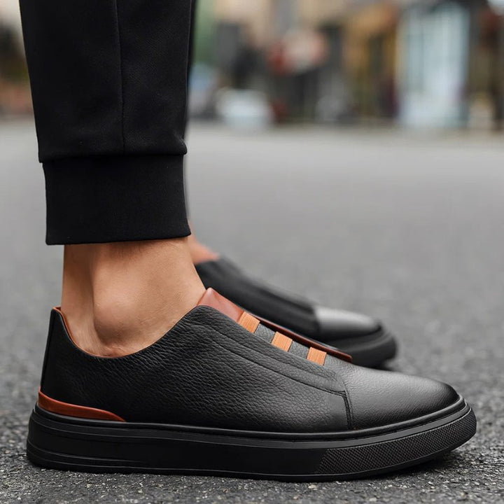 Schwarzer Herren-Sneaker aus Leder mit elastischen braunen Bändern und kontrastierender Fersendetail-Optik.