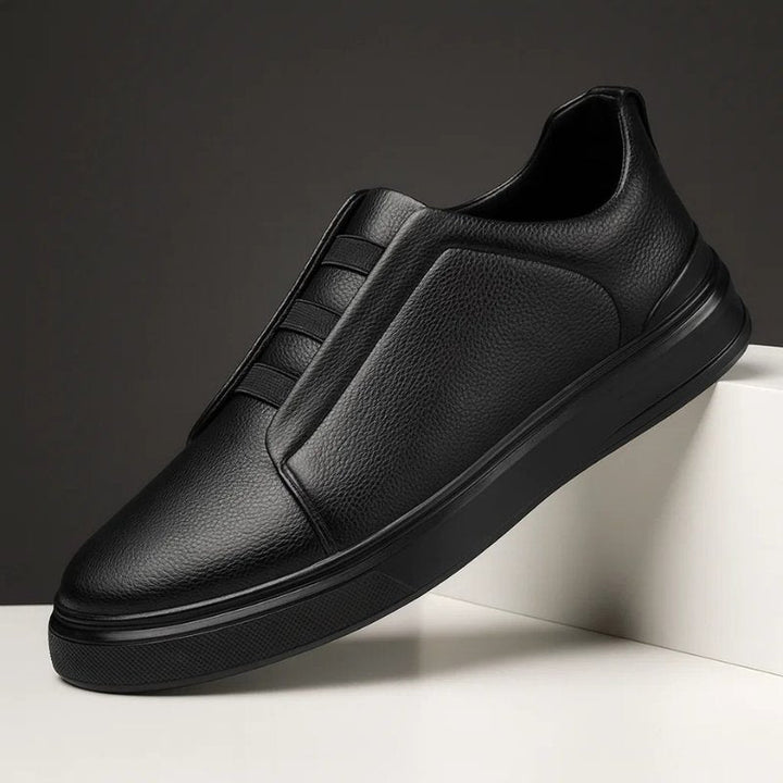Schwarzer Herren-Slip-On Sneaker aus genarbtem Leder mit elastischen Bändern und robuster Gummisohle im minimalistischen Design.