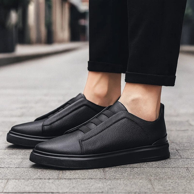 Schwarzer Herren-Slip-On-Sneaker aus genarbtem Leder mit elastischen Bändern und robuster Laufsohle.