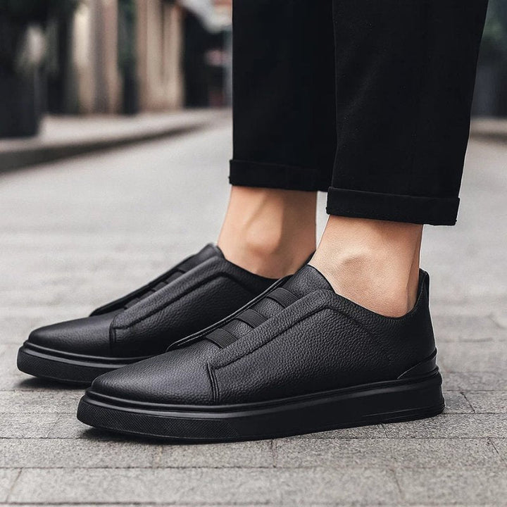 Schwarzer Herren-Slip-On-Sneaker aus genarbtem Leder mit elastischen Bändern und robuster Laufsohle.
