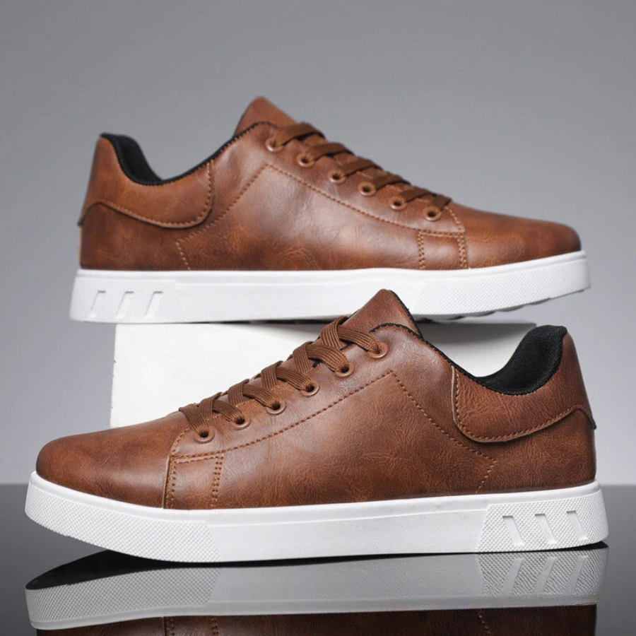 Braune Herren-Sneaker in Lederoptik mit Schnürung und kontrastierender weißer Sohle vor grauem Hintergrund.