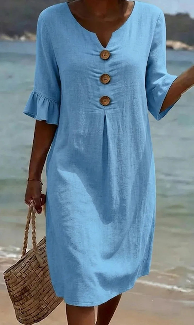 Hellblaues Fiona Midikleid mit V-Ausschnitt, Volant-Ärmeln und Zierknöpfen am Strand.
