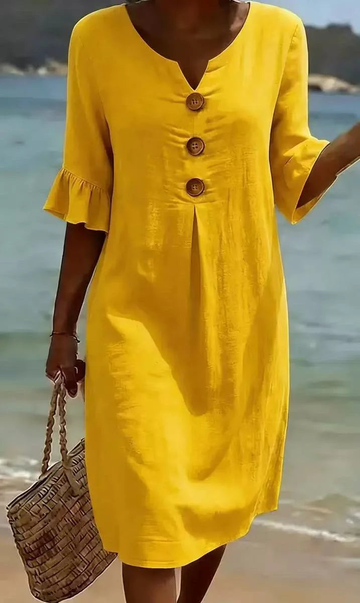 Gelbes Fiona Midikleid mit V-Ausschnitt, Volant-Ärmeln und dekorativen Holzknöpfen am Strand.