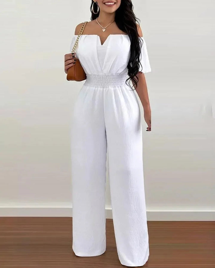 Weißer Off-Shoulder Jumpsuit mit weitem Bein, betonter Taille und fließendem Stoff für einen eleganten Look.