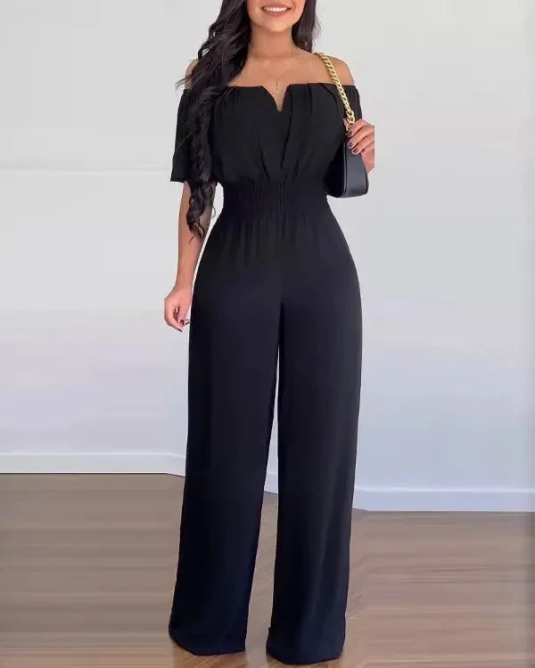 Schwarzer Greta Jumpsuit mit Off-Shoulder-Ausschnitt, betonter Taille und fließendem, weitem Bein.