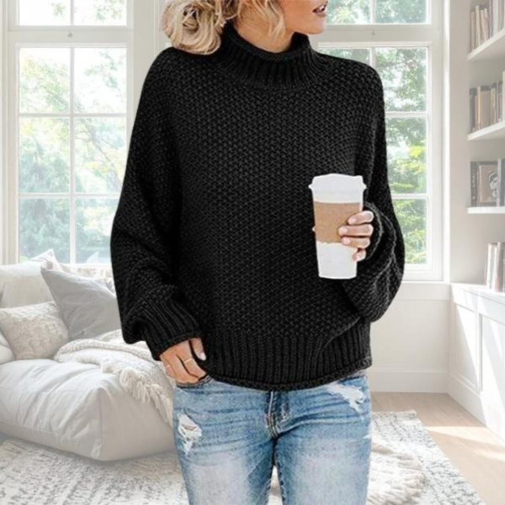 Schwarzer Damen-Grobstrickpullover mit Rollkragen, lockerer Passform und gerippten Bündchen in gemütlichem Wohnzimmer-Ambiente.