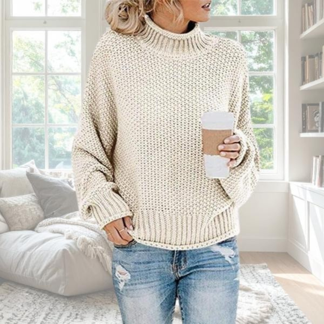 Beiger Damen-Grobstrickpullover mit hohem Rollkragen, lockerer Passform und gerippten Bündchen in gemütlichem Wohnzimmer.