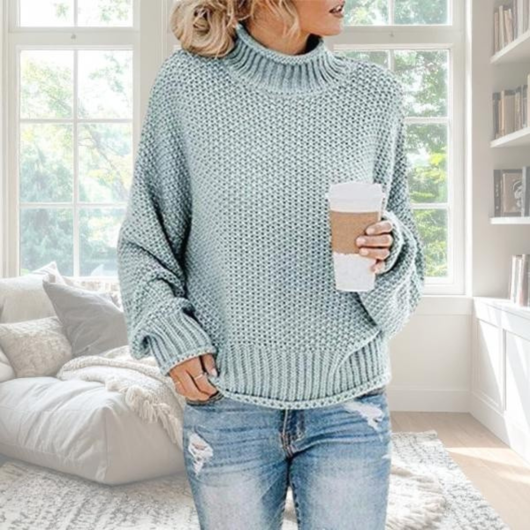 Hellblauer Damen-Grobstrickpullover mit Rollkragen, lockerer Passform und gerippten Bündchen in gemütlichem Wohnzimmer.