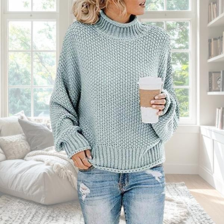 Hellblauer Damen-Grobstrickpullover mit Rollkragen, lockerer Passform und gerippten Bündchen in gemütlichem Wohnzimmer.