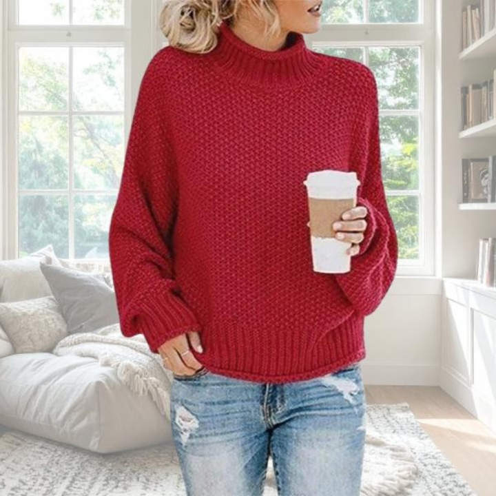 Roter Grobstrick-Pullover mit Rollkragen und relaxter Passform, kombiniert mit Jeans in einem gemütlichen Wohnzimmer.
