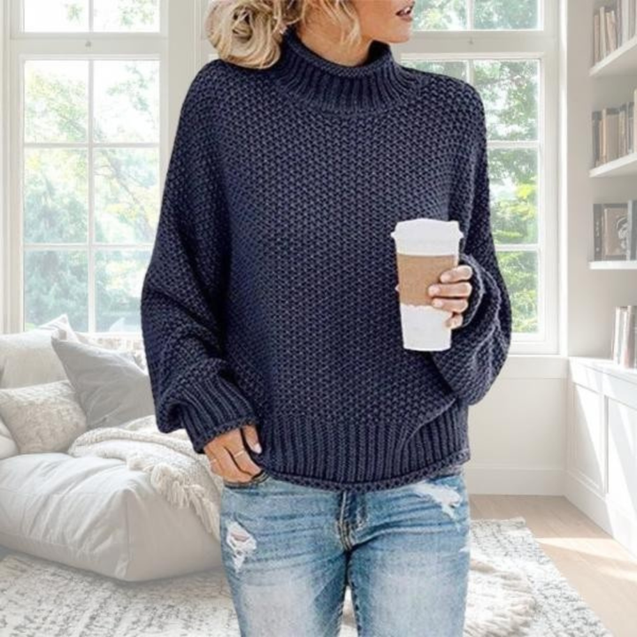 Dunkelblauer Damen-Grobstrickpullover mit Rollkragen, lockerer Passform und gerippten Bündchen in gemütlicher Wohnumgebung.