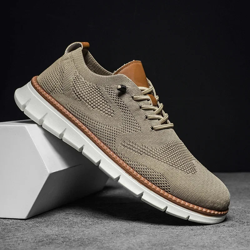 Beiger Herren-Mesh-Sneaker mit Schnürung, braunen Lederdetails und flexibler weißer Laufsohle auf einem weißen Block.