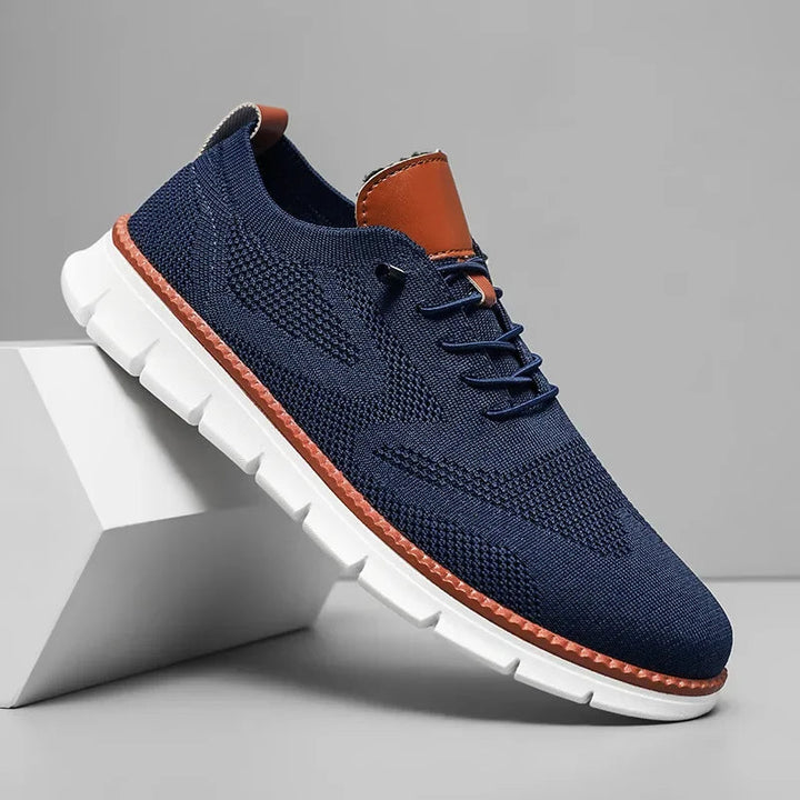Dunkelblauer Herren-Mesh-Sneaker mit braunen Lederdetails, Schnürung und weißer, flexibler Laufsohle.