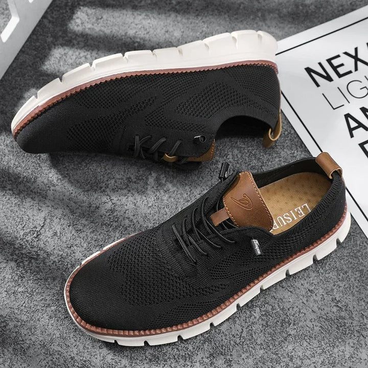 Schwarzer Herren-Sneaker aus atmungsaktivem Mesh mit braunen Lederdetails, Schnürung und flexibler weißer Laufsohle.
