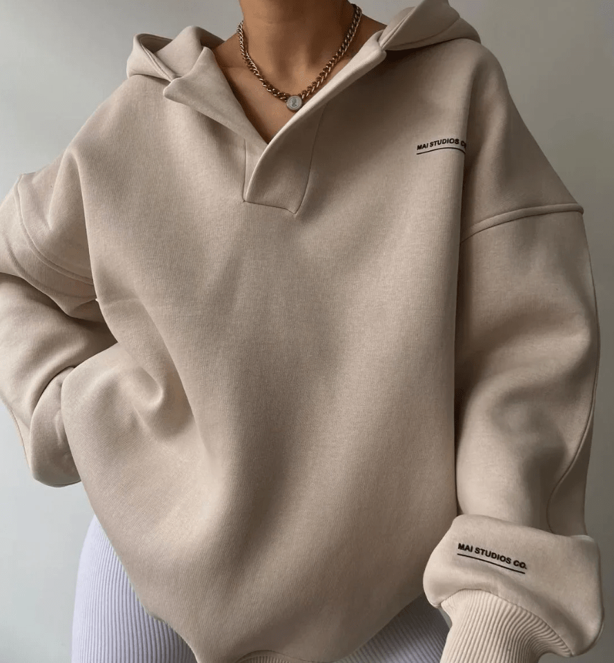 Beiger Oversized-Hoodie mit V-Ausschnitt, überschnittenen Schultern und dezentem Logo-Print an Brust und Bündchen.