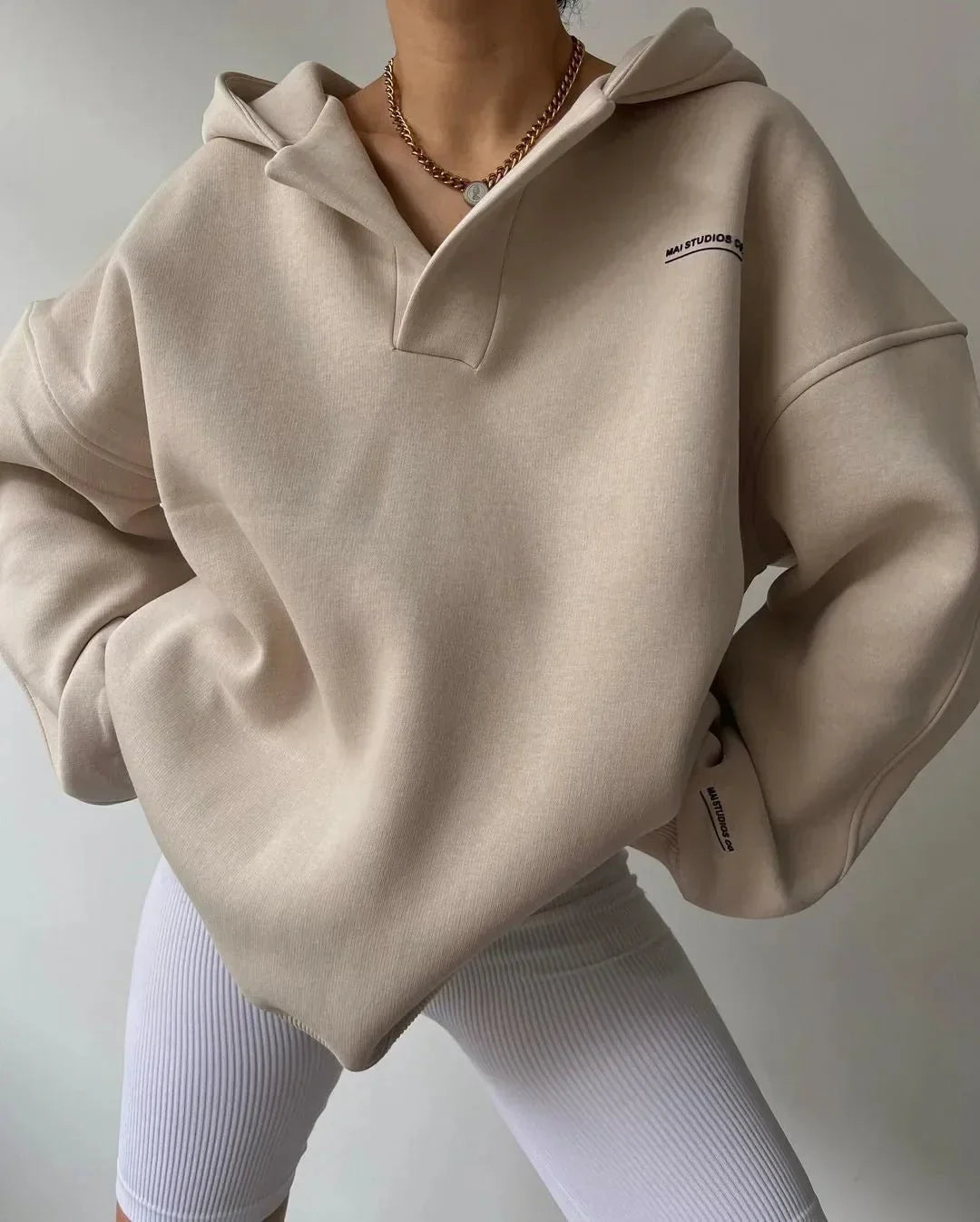 Beiger Oversized-Hoodie mit V-Ausschnitt, überschnittenen Schultern und dezentem Brust-Print.