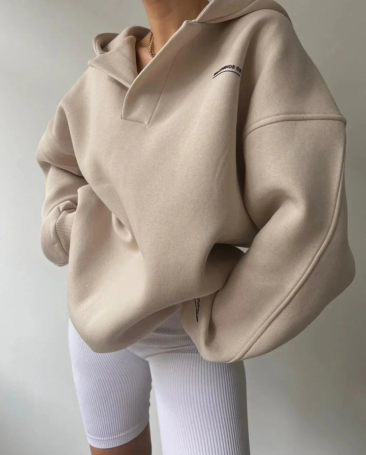 Beiger Oversized-Hoodie mit V-Ausschnitt, überschnittenen Schultern und dezentem Brust-Print kombiniert mit weißer Radlerhose.