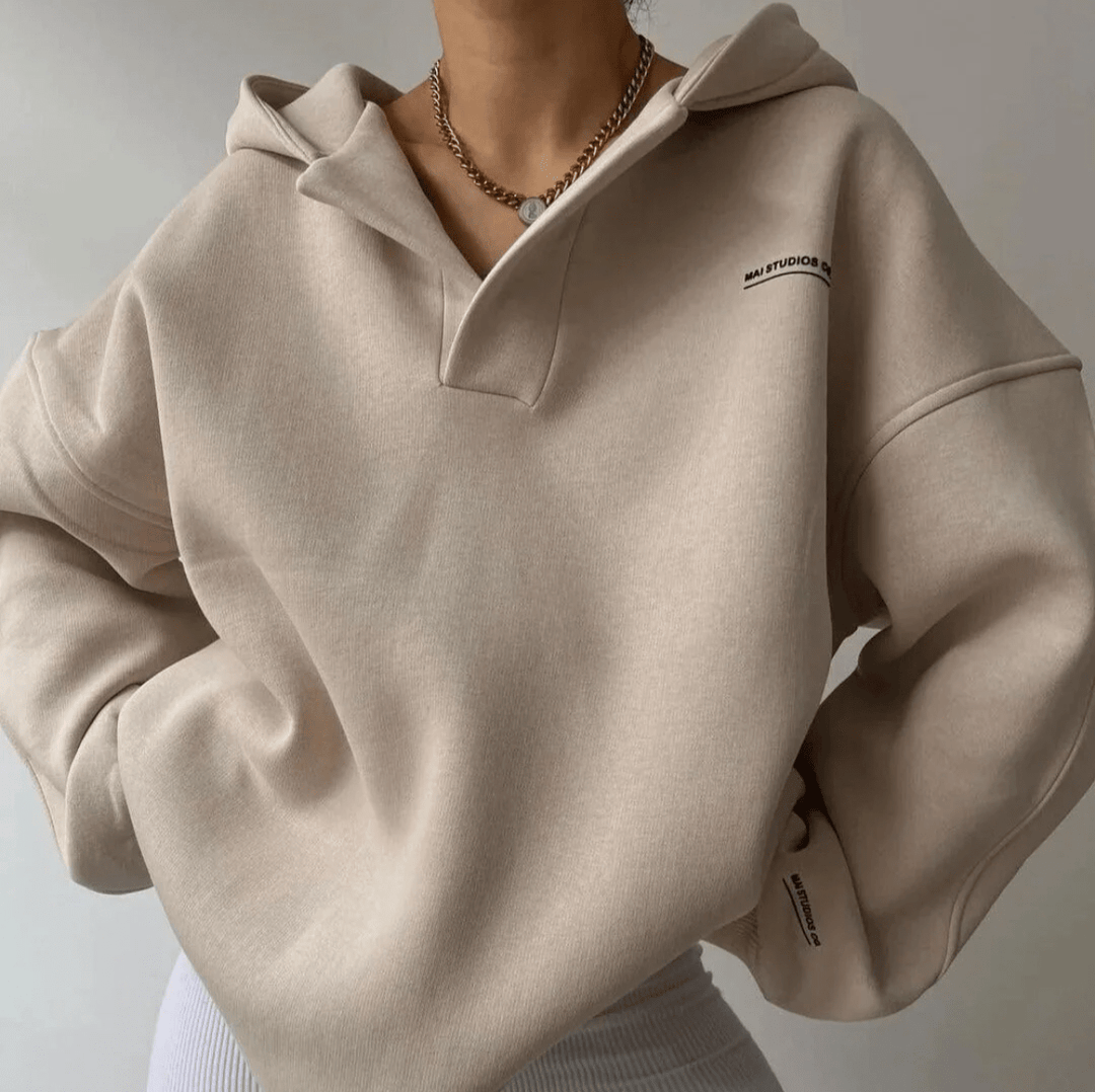Beiger Oversized-Hoodie mit V-Ausschnitt, Drop-Shoulder-Schnitt und dezentem Text-Print auf Brust und Ärmelbündchen.
