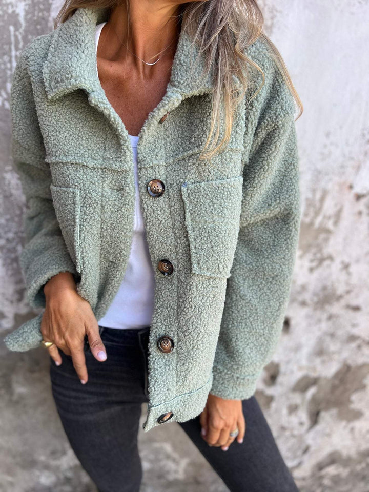Salbeigrüne Teddyjacke aus flauschigem Material mit Knopfleiste, Umlegekragen und zwei Brusttaschen.